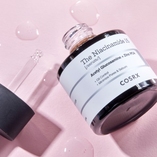 Een huidverzorgingsproduct genaamd The Niacinamide 10%, met pipet en gemorste vloeistof op een roze oppervlak.