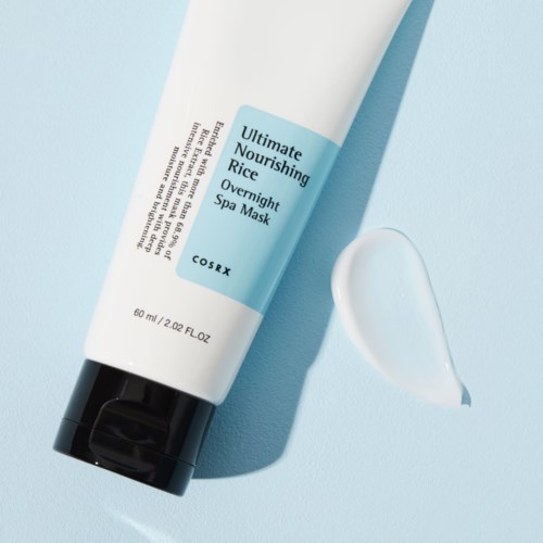 Eine weiße Tube mit dem Titel 'Ultimate Nourishing Rice Overnight Spa Mask' und etwas Creme daneben auf einem blauen Hintergrund.