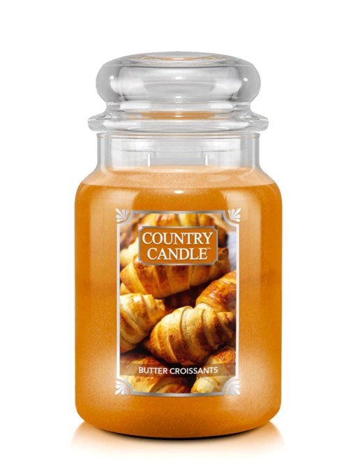 A candle in a glass jar labeled 'Country Candle' with an image of croissants, scent is butter croissants.