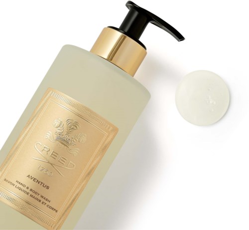 En flaske med lotion eller flytende såpe med svart pumpe, gullfarget etikett og litt krem ved siden av.