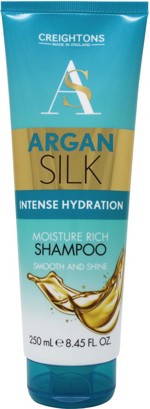 A blue and gold bottle of Argan Silk shampoo, labeled for intense hydration and moisture, with a splash of oil on the front.