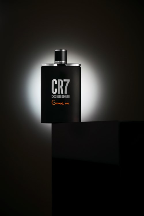Eine schwarze Parfümflasche mit weißem Text "CR7" und "Cristiano Ronaldo" beleuchtet vor dunklem Hintergrund.