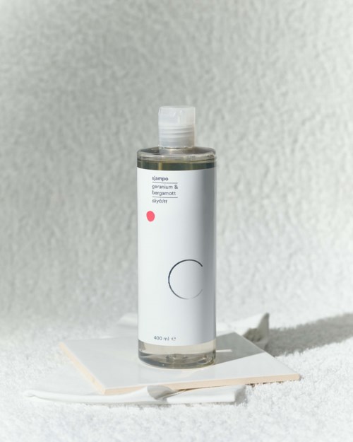 A clear bottle of shampoo with a simple white label, standing on some white paper or cloth.