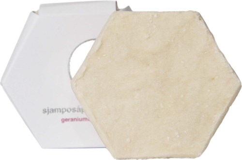 A hexagonal soap bar in front of a white box, possibly the packaging. The soap is light-colored and textured.