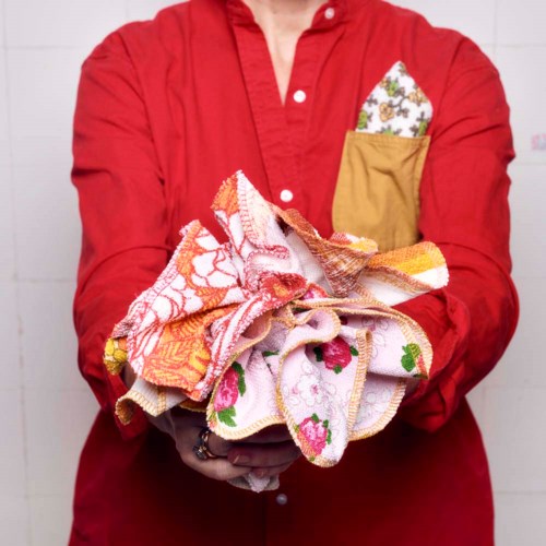 A person in a red shirt holding colorful, patterned cloths and towels, with a pocket containing a small towel.