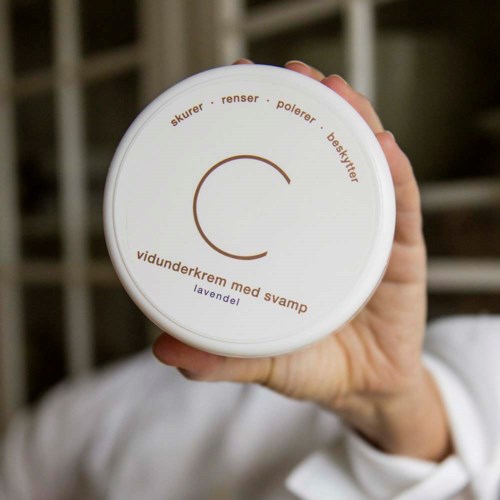 A hand holds a round container with a white lid, displaying text about skincare products in Norwegian.