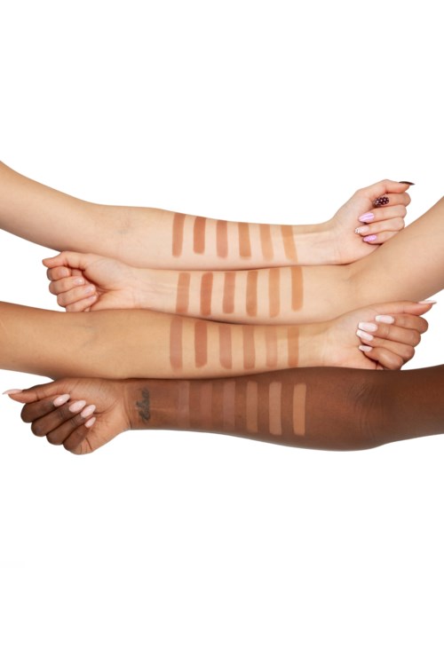 Vier armen met verschillende huidtinten tonen verschillende tinten make-up of bronzer in strepen.