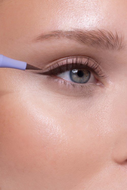 Een persoon brengt zwarte eyeliner aan op het bovenste ooglid met een kleine kwast.