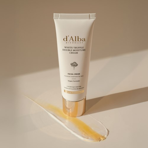 Eine weiße Tube mit d'Alba Hautcreme mit goldenen Akzenten, steht auf einer weißen Oberfläche mit einem gelben Strich.