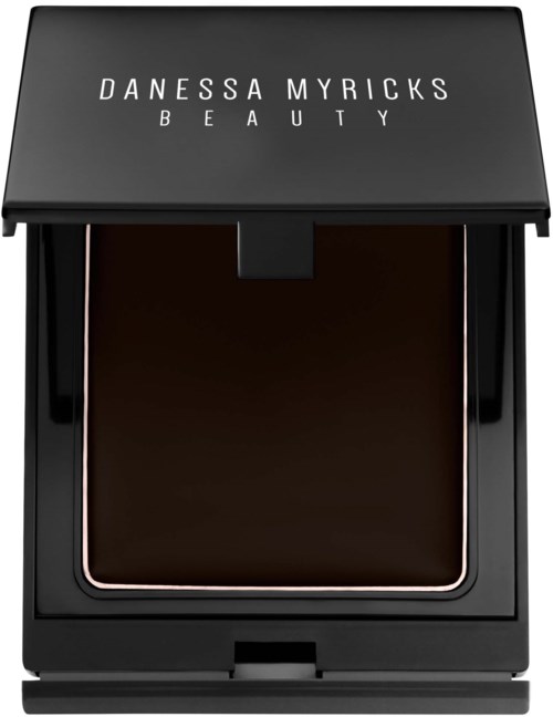 Ein schwarzer quadratischer Kompaktdeckel mit geschlossenem Deckel zeigt die Marke 'Danessa Myricks Beauty' oben. Es scheint ein Make-up-Produkt zu sein.