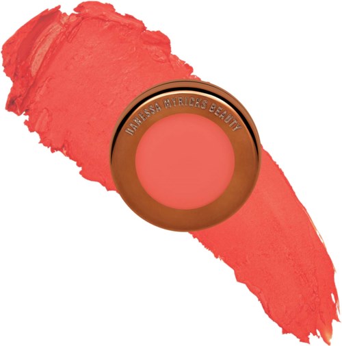 Een ronde blush met de merknaam 'Manessa Myrick's Beauty' bovenop, omgeven door roze lippenstiftvlekken.