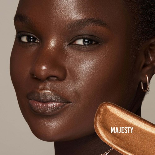 En kvinna med mörk hud håller en bronsfärgad makeup-kompakt märkt Majesty.
