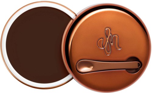 A round container with a lid showing a signature logo and a small applicator inside, filled with dark brown cream.