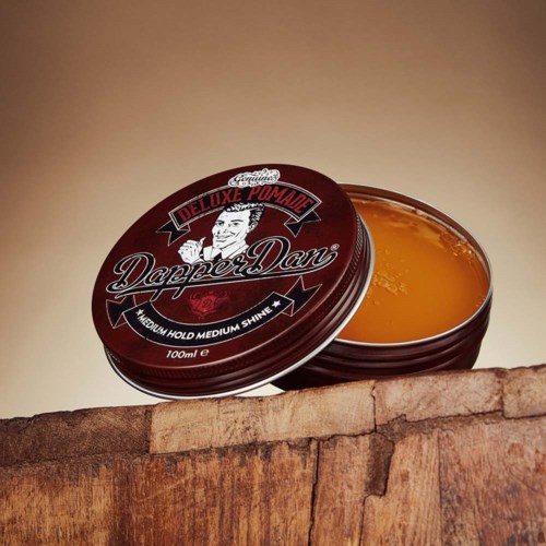 A red tin of Dapper Dan hair pomade on a wooden surface with open lid showing the product inside.