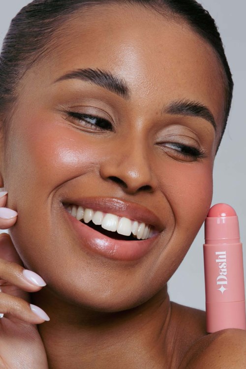 A woman smiling and holding a pink lipstick tube close to her face.