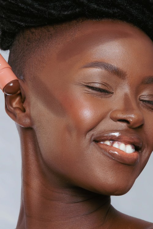 A smiling woman with closed eyes, short hairstyle, and smooth dark skin. She wears a brown earring and appears happy.