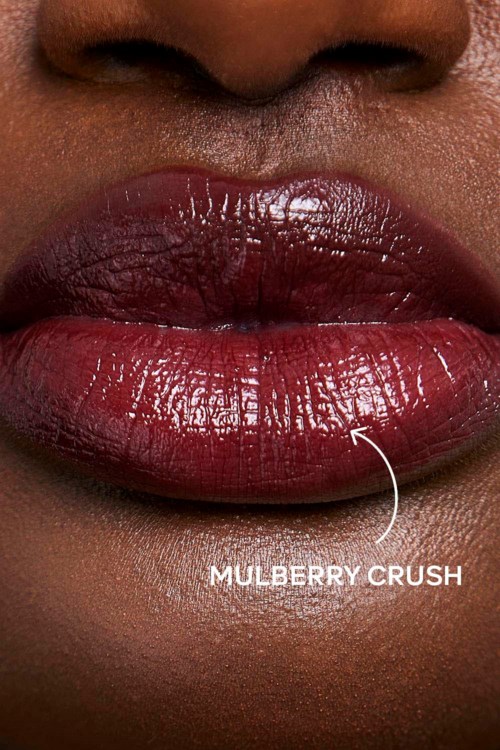 Close-up van lippen met glanzende, donkere lipstick. De tekst zegt "Mulberry Crush" op de lippen.