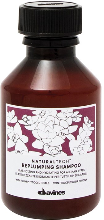 En liten brun flaska med svart lock, märkt som Replumping Shampoo för alla hårtyper, med blomsterdesign.
