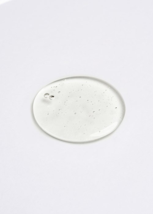 A clear, round drop of liquid on a white surface, with tiny bubbles and particles inside.