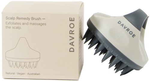 A scalp brush with black bristles and a white handle, beside its box with simple line drawing and text.