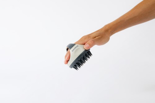 A hand holds a gray brush with black bristles, used for cleaning surfaces.