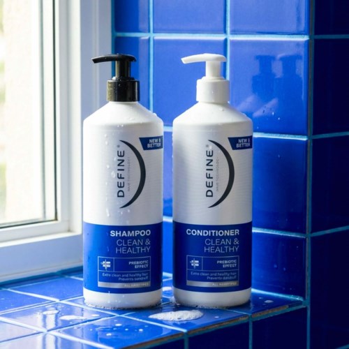 Two white bottles of shampoo and conditioner stand on blue tiled bathroom counter near window.