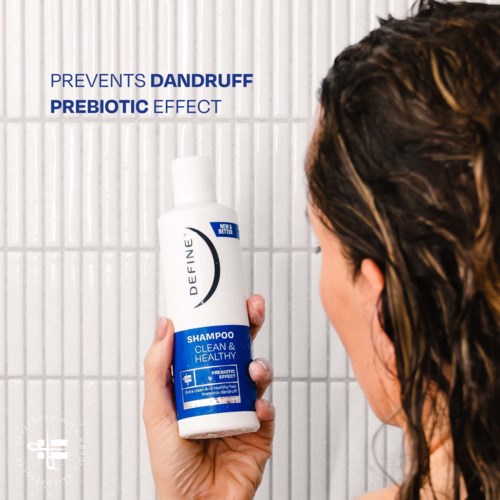 A woman holding a shampoo bottle that prevents dandruff and has probiotic effects in a bathroom.