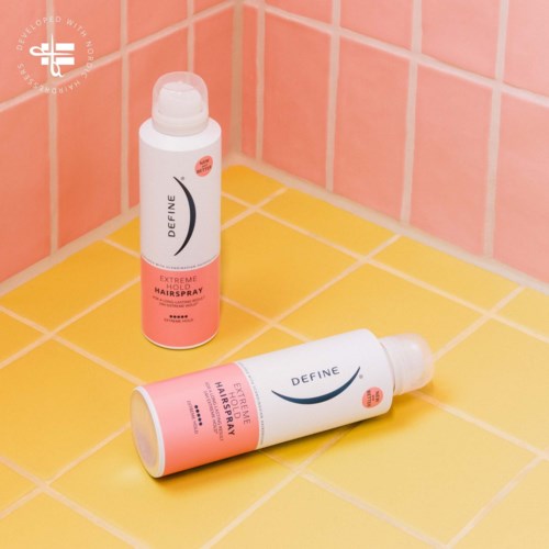 Two bottles of hair spray on yellow and pink tiled floor in a bathroom corner.