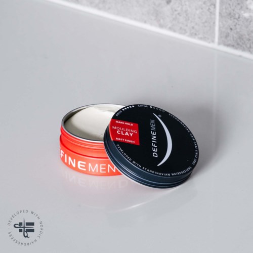 Twee metalen blikken, eentje met een rode label en de andere zwart, liggen op een witte ondergrond naast een betegelde muur.