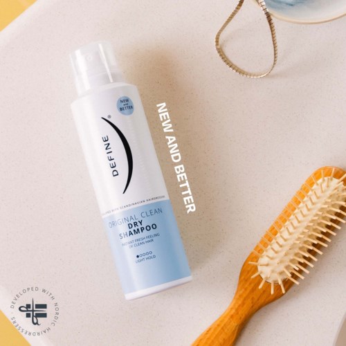 A bottle of dry shampoo, a hairbrush, and part of a mirror on a white surface.