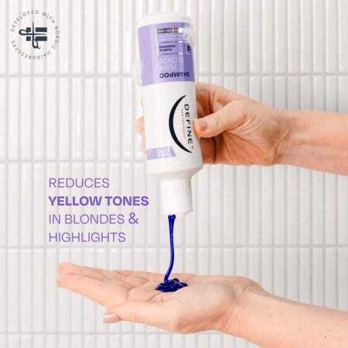 A hand holds a purple bottle of shampoo with blue liquid pouring out, against a white tiled background.