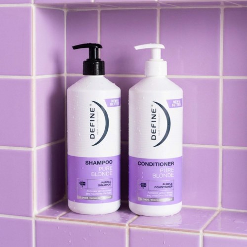 Two bottles of shampoo and conditioner are placed on purple tiled wall corner.