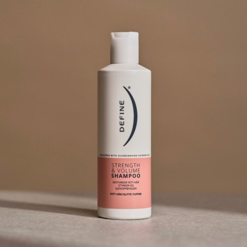 En hvit flaske med styrke- og volumshampoo med rosa etikett, plassert på en overflate.