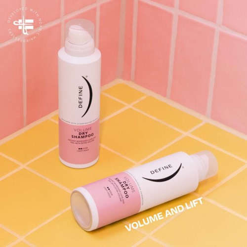 Two bottles of dry shampoo on a yellow tiled surface, with pink tiled wall in background. Text says volume and lift.