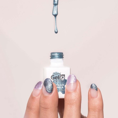 Hands with purple and silver nail polish holding a small white bottle of gel nail polish, with a drop falling into the bottle.
