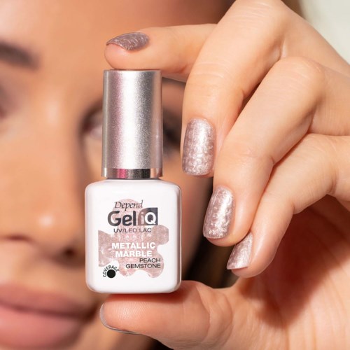 Person holding a bottle of metallic peach nail polish with glittery nails visible.