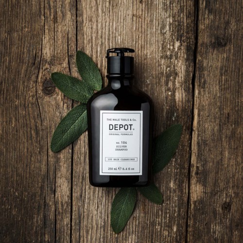A black bottle of men's shampoo on wooden background with green leaves around it.