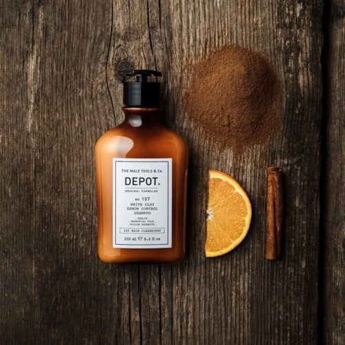 A brown bottle of beard wash, orange slice, brown powder, and a cinnamon stick on wooden surface.
