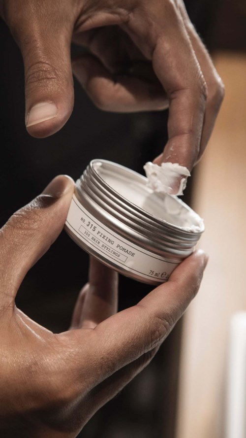 Hender som åpner en beholder med hvit krem eller lotion. Fokuserer på fingre og beholder, med uskarp bakgrunn.