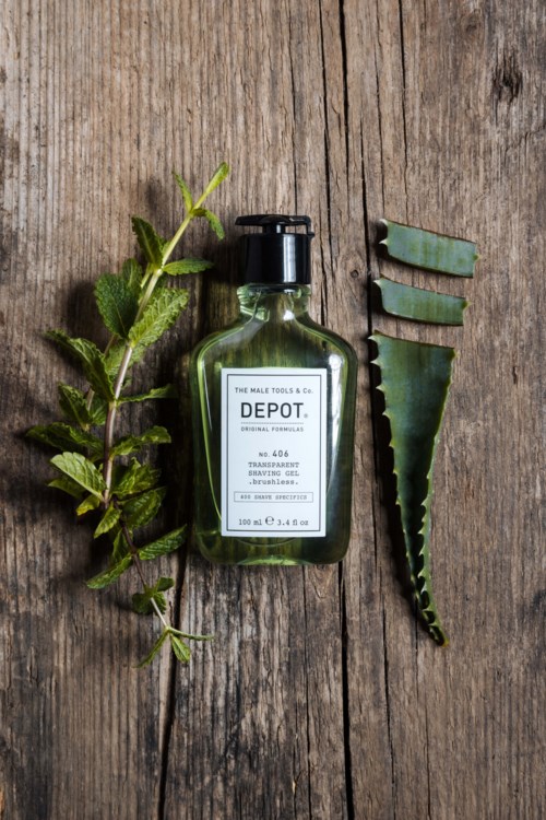 Vihreä DEPOT-shavesuihke, vihreitä aloe vera -lehtiä ja yhä aloe lehden puulattialla.