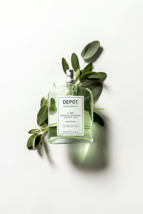 A clear perfume bottle with green leaves around it on a white background.