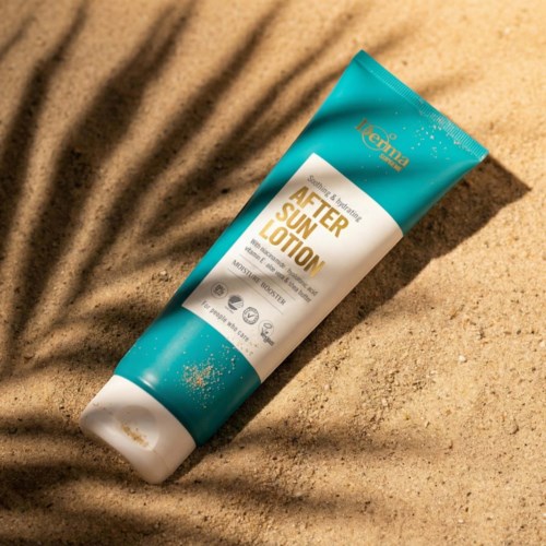 A blue and white tube of after sun lotion on sandy ground with shadow patterns.