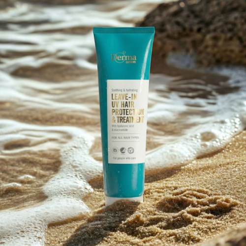 A turquoise and white tube of leave-in spray stands on the sandy beach with water and rocks in the background.