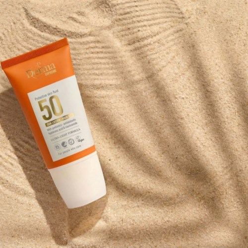 Sunscreen tube labeled SPF 50 is on sandy ground, casting a shadow in bright sunlight.