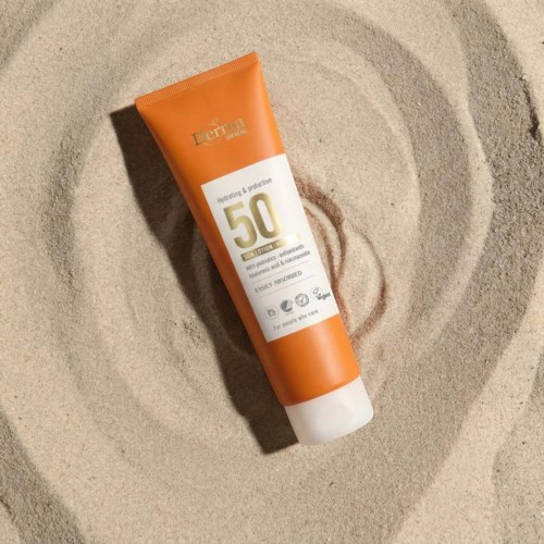 An orange sunscreen tube with SPF 50 lies on sand, surrounded by heart-shaped sand patterns.
