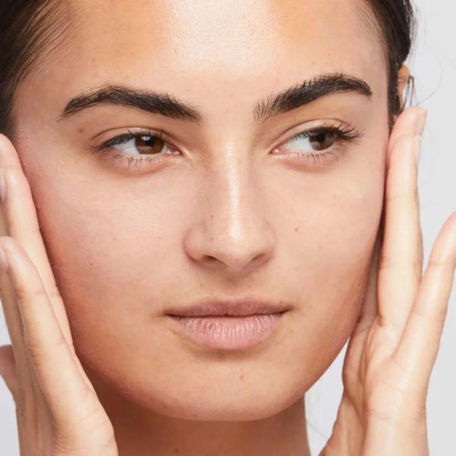 Een vrouw raakt voorzichtig haar gezicht aan, met een schone huid en natuurlijke make-up, ziet er kalm en ontspannen uit.