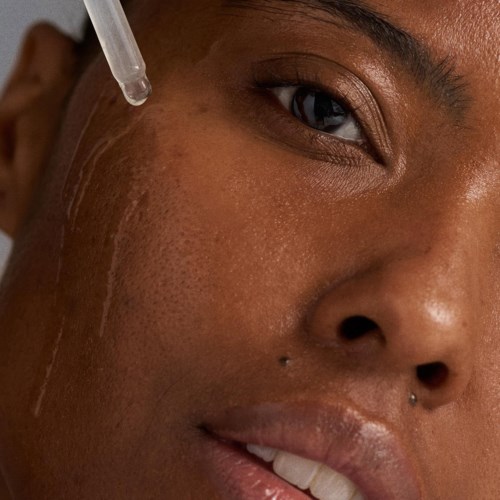 Eine Person erhält Hautpflege mit einer Pipette über der Wange, Nahaufnahme des Gesichts und Augendetails.
