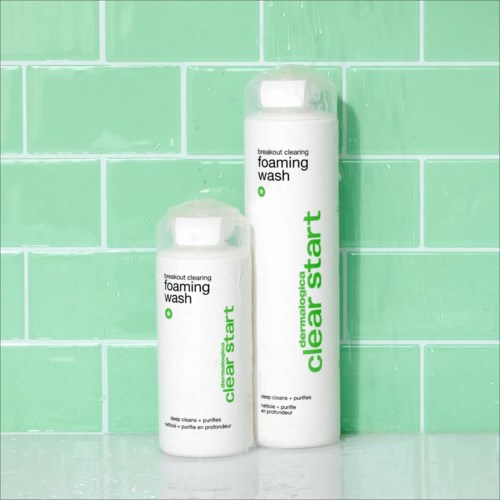 Twee flessen van clear start schuimende was staan op een oppervlak voor een groene betegelde muur.