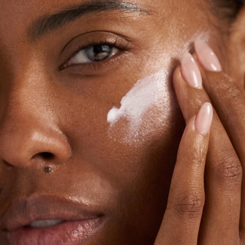 Eine Person trägt weiße Creme auf die Wange auf mit den Fingern, Fokus auf Hautpflege oder Schminke.