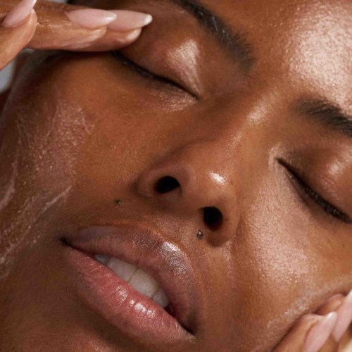 A person is enjoying a facial skin care routine, applying a product to their face with their hand.